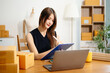 © laddawan - Asian young woman SME working using smartphone or tablet taking receive and checking online purchase shopping order