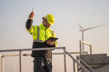 Fototapete - Engineer man working with tablet at windmill farm Generating electricity clean energy. Wind turbine farm generator by alternative green energy.