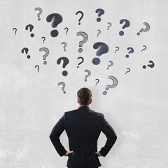 Fototapete - Businessman standing with hands on hips facing a wall of scattered question marks, symbolizing confusion and decision-making in business.