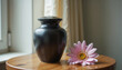 © Arra Vais - Elegant pet urn in matte black finish with a single flower beside it on a wooden table