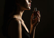 © Gita - Woman in a black dress holding a perfume bottle close to her neck, captured with dramatic low light for a sensual and intimate mood.