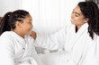 © Prostock-studio - Cheerful African American Mom And Daughter In Bathrobes Sitting On Bed, Relaxing After Home Spa Day. Loving Black Mother And Her Child Having Fun Together, Laughing And Chatting, Free Space