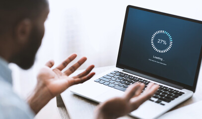 slow computer software concept. indignant african american guy looking at laptop with loading screen