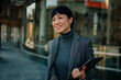 © Zamrznuti tonovi - Smiling businesswoman holding tablet and walking in city center
