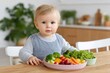 © kardaska - Baby eating healthy vegetables sitting in high chair in kitchen