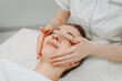 © Anton Pentegov - face massage, young attractive caucasian woman, beautiful relaxed lady with closed eyes smiling, white towel, spa therapist doing facial and head massage in beauty salon, skincare and bodycare concept