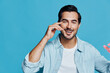 © SHOTPRIME STUDIO - Smiling man wearing a light blue shirt, showcasing a cheerful expression while gesturing playfully against a bright blue background. Portrait with positive vibes.