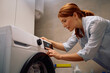 © Drazen - Happy woman adjusting timer on washing machine while doing laundry,