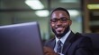© Pedro - Bearded black businessman in suit smiling in front of computer