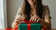 © Igorbmm - A smiling woman tying a vibrant red ribbon on a green gift box at a table. Mother's Day.