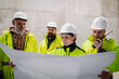 © Halfpoint - Team of engineers and construction workers reviewing blueprints, building site.