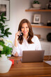 © gzorgz - Brunette haired businesswoman siting at home and using cell phone and laptop