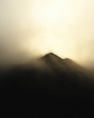Wall Mural - Ethereal mountain peak shrouded in mist under a warm golden sky creating a sense of mystery and adventure with a minimalist and dramatic composition