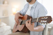 © New Africa - Man playing guitar at home, focus on hand