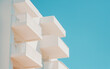 © TheseusStock - Close-up photo of a white apartment building with balconies, against a blue sky background, on a bright, sunny day in summer