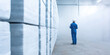 © dinastya - Worker in blue uniform standing in a large warehouse surrounded by stacks of boxes. Industrial storage and logistics