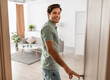 © Prostock-studio - Portrait of excited young man walking in his apartment, entering new home and looking back at camera, happy young guy standing in doorway of modern flat, coming inside, selective focus
