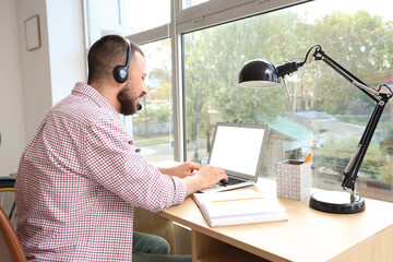 Wall Mural - freelancer sitting at workplace with headset and laptop at home
