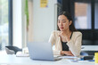 © amnaj - Young asian businesswoman working with laptop and analyzing financial data while sitting at her desk in modern office