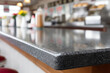 © Olha Havelia - A close-up shot of the countertop in an American diner, showcasing its shiny black granite surface with subtle speckles and shimmering reflections. In the background, various items