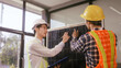 © NanSan - Two Asian businessmen wearing engineer hats table, discussing solar panels and wind turbines. They plan environmental projects, focusing on solar energy solutions and renewable energy installations