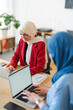© Studio Marmellata - Two women in hijabs are collaborating on a project. They're using laptops and notebooks to brainstorm and work together, likely to achieve a shared goal in a professional setting.