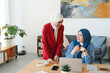 © Studio Marmellata - Two smiling women in hijabs collaborate on a project at a desk. They're likely working together on a business or creative endeavor, enjoying the process and each other's company.