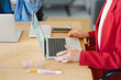 © Studio Marmellata - A woman in a red blazer works on her laptop at a wooden desk. She's likely preparing for a meeting or working on a project with colleagues nearby.