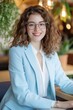 © Amanda - Young professional woman smiling in office setting with plants, wearing glasses and business attire, engaged in work and collaboration on a project.