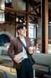 © bongkarn - Brown suit man with glasses standing while holding a coffee cup and notebook in cafe or coffee shop.