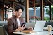 © bongkarn - Brown suit asian man with glasses is looking at his smartphone while sitting in cafe or coffee shop.
