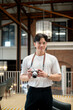 © bongkarn - Asian man wearing glasses in white t shirt is standing and holding his camera in cafe or coffee shop