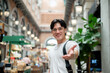 © bongkarn - Asian man wearing glasses posing with extending a hand in hallway of shopping mall or indoor market.