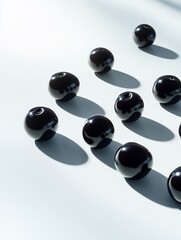 Poster - Shiny black berries arranged on a white surface, casting shadows.
