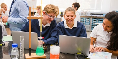 Fototapete - Students in a science lab working on laptops. Chemistry equipment on the table. Engaged students, collaborative learning, science education in action. Diverse students in science class.