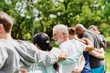 © Rawpixel.com - Elderly man and diverse people hugging each other. Diverse group of women and men embrace each other at park. Unity and teamwork. Backside of old man and friends standing in row huddle on green grass.