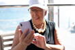 © luciano - Elderly 80-year-old retired woman in elegant casual dress happily looks at smartphone. Her expressions convey happiness and positivity, elderly grandmother stays connected in the digital age