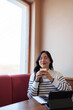 © crizzystudio - Young woman sits in a cafe, savoring the aroma of her coffee with closed eyes, a tablet and notebook resting on the table beside her, suggesting a moment of peaceful relaxation amidst a busy day