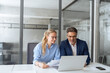 © Stock 4 You - Mature mentor senior leader man, young woman manager discussing project on laptop in modern office. Two partners, colleagues, team of professional finance specialist business people working at desk