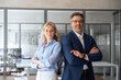 © Stock 4 You - Portrait of confident mature leader man and young employee woman manager standing in office, looking proud at camera. Two diverse colleagues, group team of professional business people at workplace