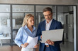 © Stock 4 You - Mature mentor senior leader man, young woman manager discussing project on laptop in modern office. Two partners, colleagues, team of professional finance specialist business people working together
