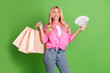 © deagreez - Smiling young woman holding shopping bags and cash in hand wearing pink shirt posing on a green background