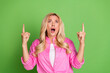 © deagreez - Surprised Young Woman in Pink Shirt Pointing Upward Against Green Background Expressing Excitement and Performing Gestures
