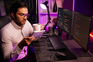 Smart IT developer working with coffee on software development coding on pc screen, reading note with newest application project program update online website data at neon light cyber office. Surmise.