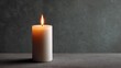 © CYBERPINK - Close-up of a single white candle on a grey surface. the candle is lit, with the flame burning brightly. the background is a dark grey color, creating a contrast with the bright orange flame.