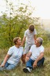 © Serhii - Grandson, grandfather and grandmother sitting on grass having fun outdoors in park at sunset