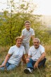 © Serhii - Grandson, grandfather and grandmother sitting on grass having fun outdoors in park at sunset