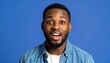 © Shousei - 30代アフリカ系アメリカ人男性がディープブルー背景の前で、驚きと興奮を表現する開いた目と口のクローズアップ