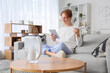 © Pixel-Shot - Young man with glass and water filter jug using tablet computer on sofa at home