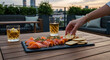 © DEGE - Smoked salmon served on black slate with dill, person’s hands placing crackers, rooftop dining setting.
